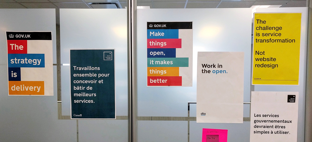 Posters on the wall of a government office, saying: “The strategy is delivery,” “Travaillons ensemble pour concevoir et bâtir de meilleurs services,” “Make things open, it makes things better,” and other catchphrases.