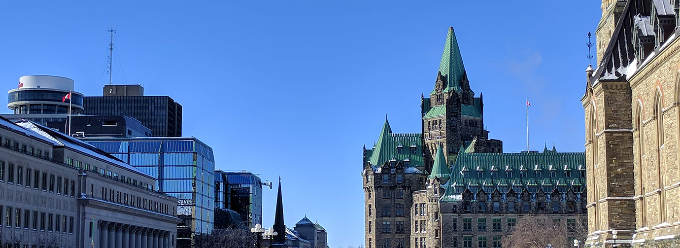 A photo from near Parliament Hill looking west at the Confederation Building and other buildings along Wellington, on a sunny February day.