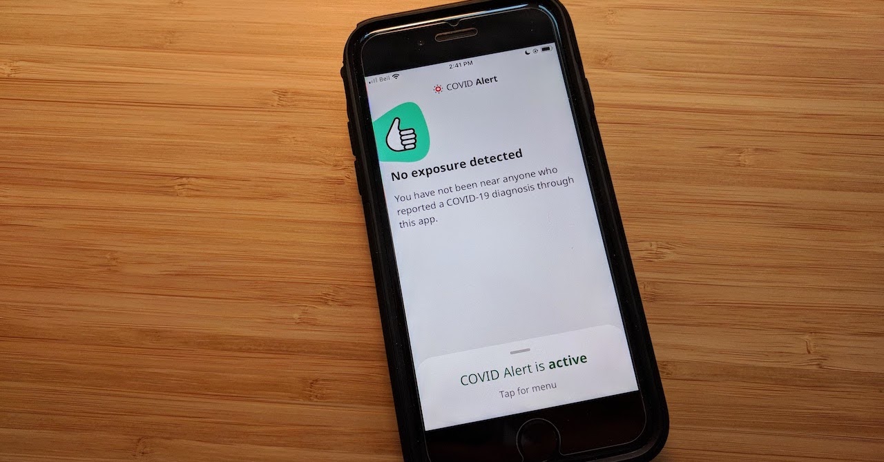 An iPhone on a wood-panel desk, showing the COVID Alert app with a message that says “No exposure detected”.