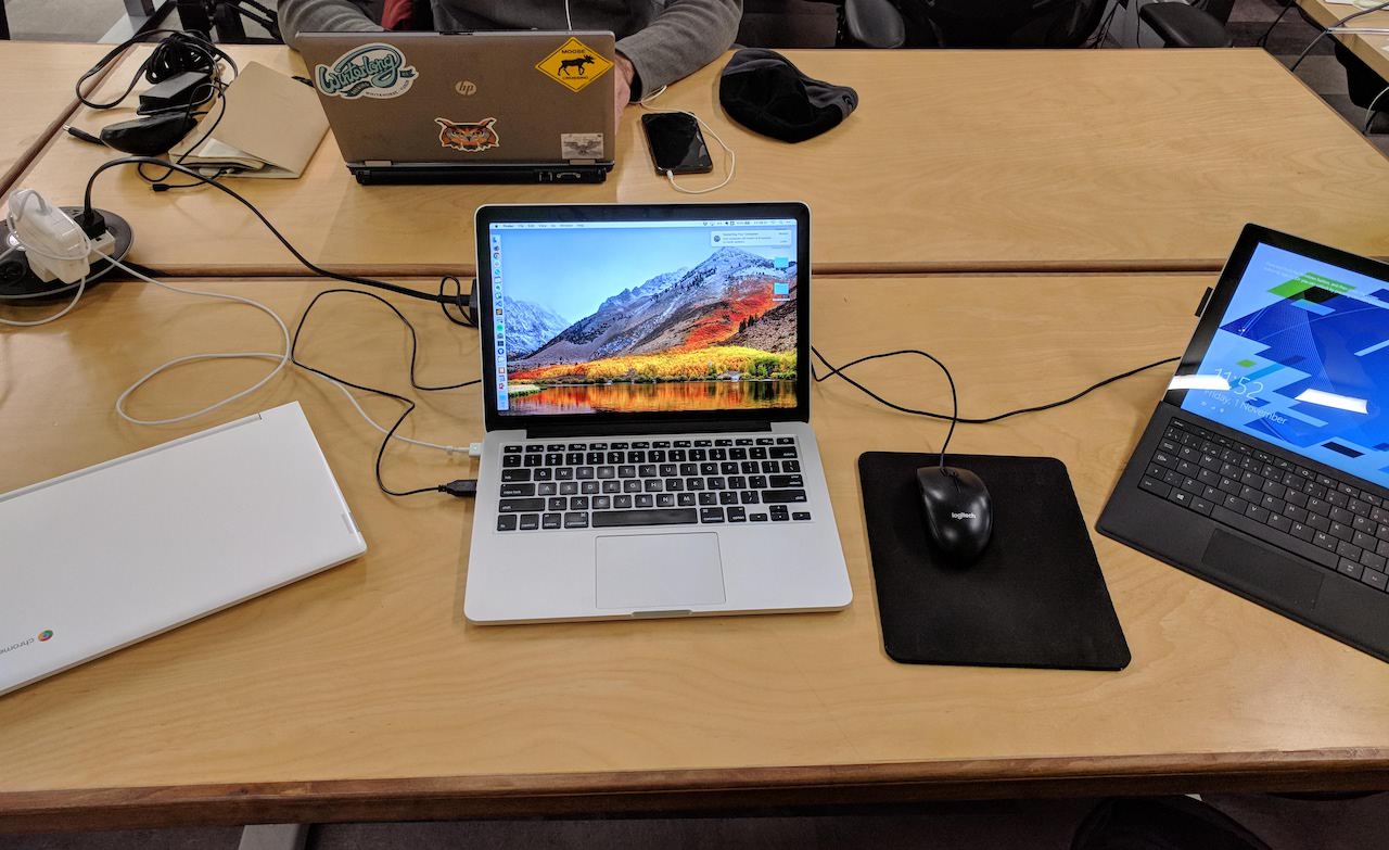 Three different kinds of laptop computers (a Chromebook, a MacBook, and a Surface Pro tablet) all open next to each other on a desk.