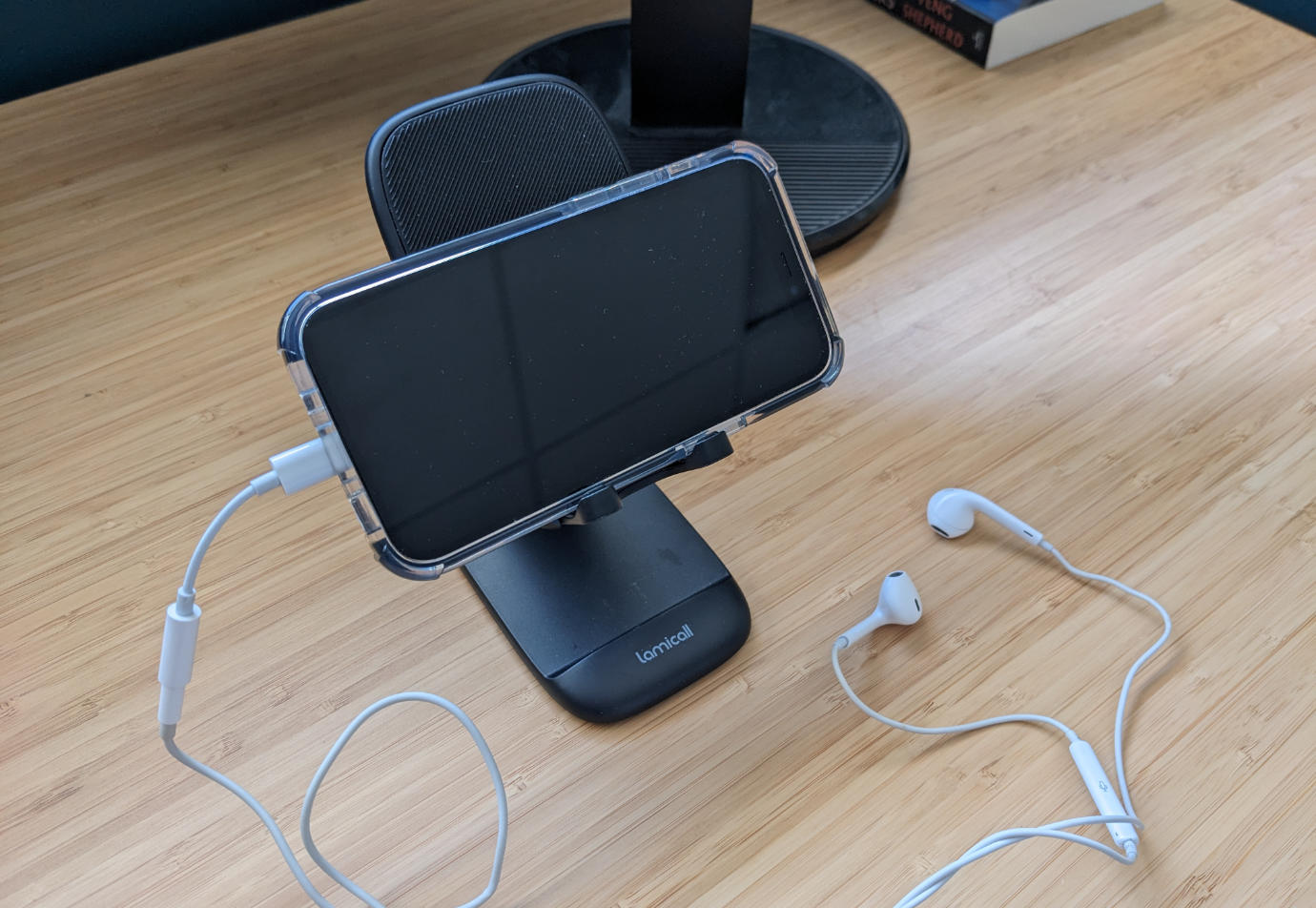 An iPhone sitting on a portable phone stand with a Lightning-to-headphone jack adapter and wired headphones plugged into it.
