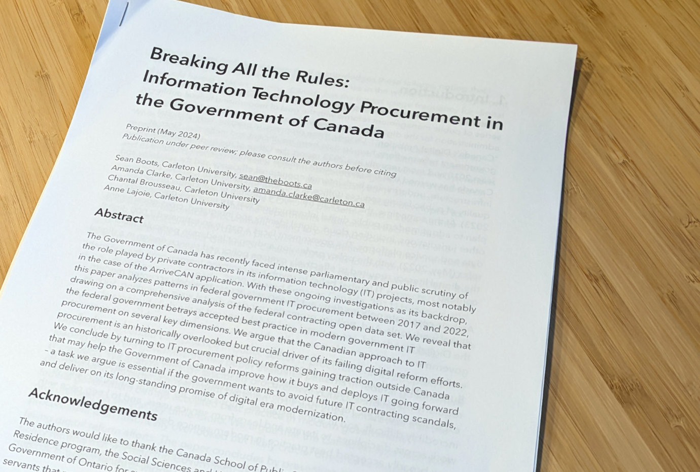 A photo of a paper copy of the research paper, titled “Breaking All the Rules: Information Technology Procurement in the Government of Canada”, sitting on top of a wooden desk.